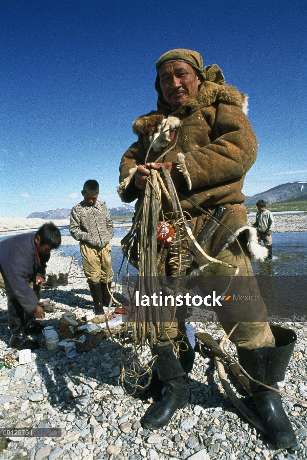 Herder de caribú (Rangifer tarandus) descansando junto a un río con su familia, Siberia, Rusia