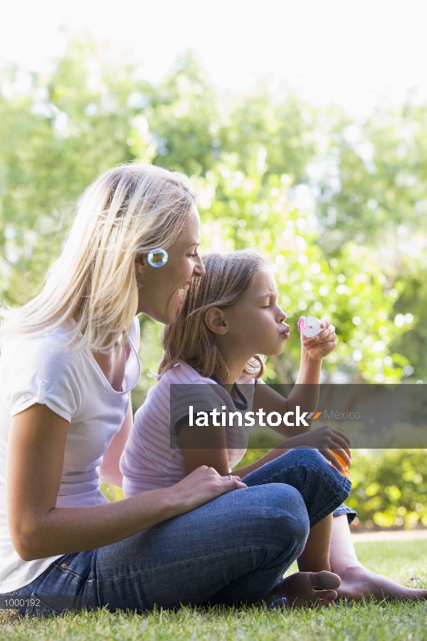 Madre e hija al aire libre soplando burbujas sonriendo